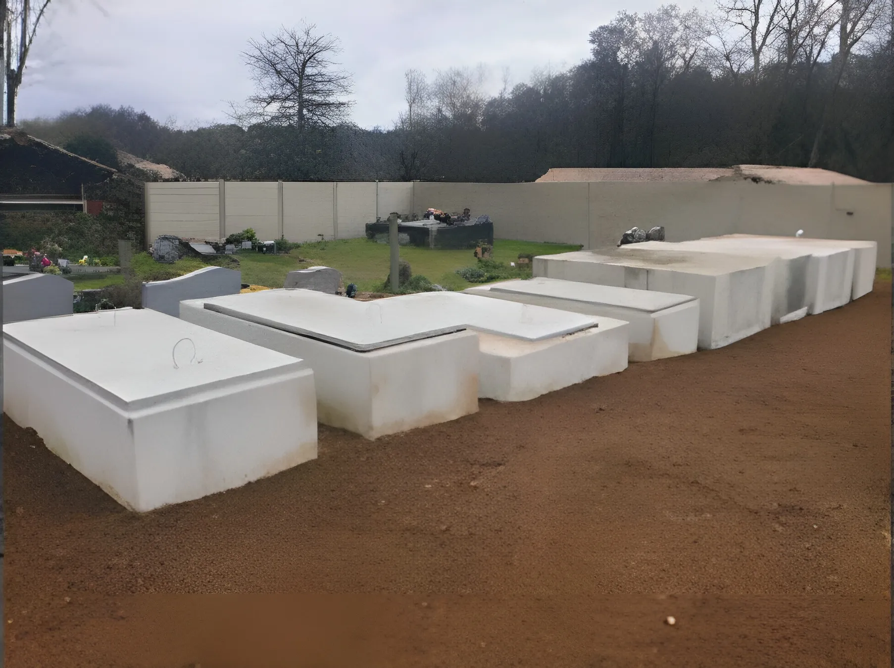 Alignement de caveaux en béton blanc fraîchement posés sur terre rouge dans un cimetière, travaux réalisés par Aquitaine Marbrerie