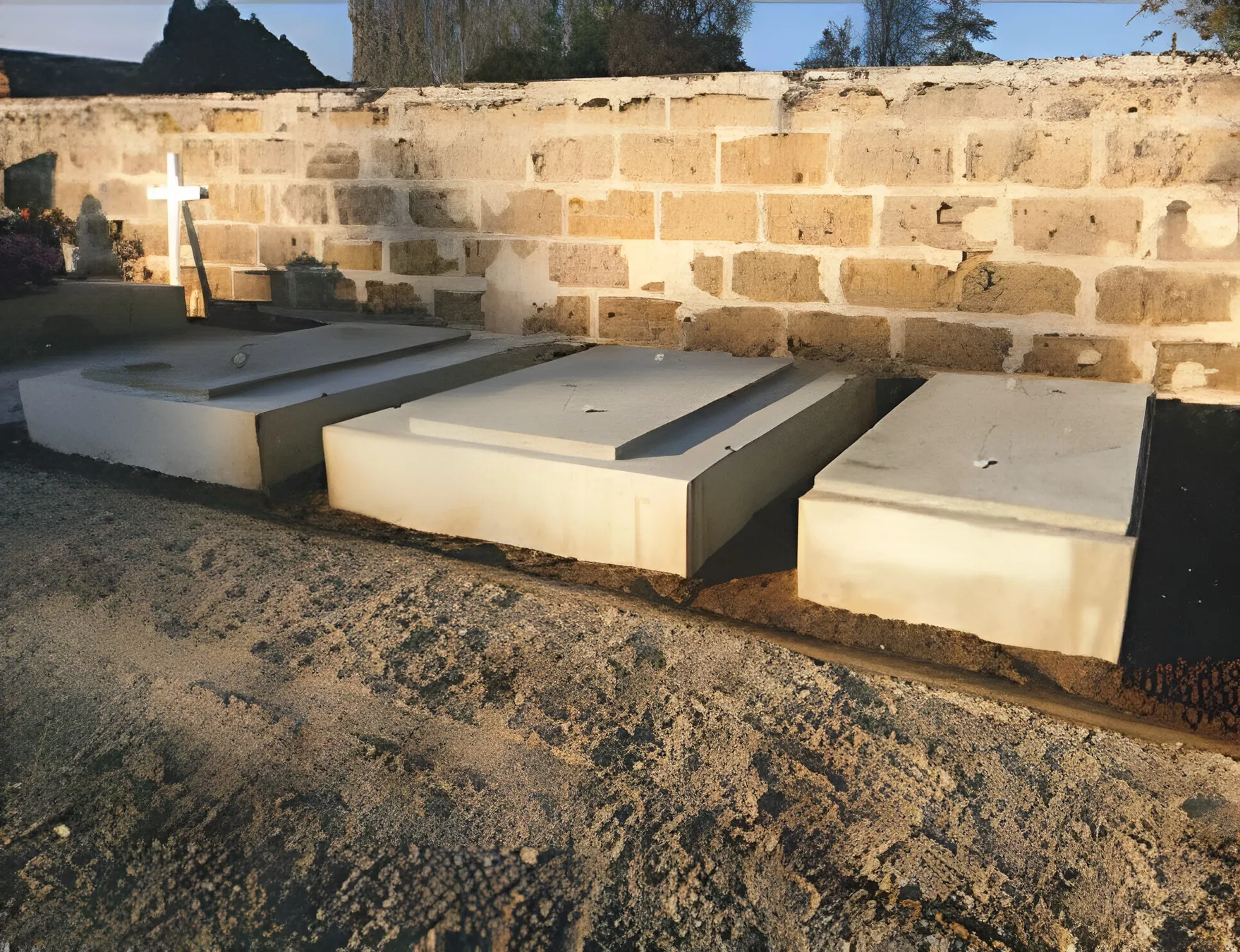 Trois caveaux en béton posés en alignement contre un mur en pierre dans un cimetière, réalisation Aquitaine Marbrerie